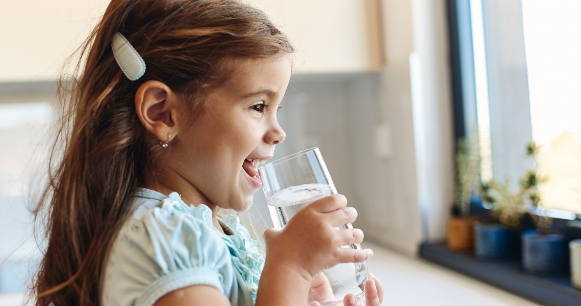 A little girl happily drinks water from a glass, choosing it over a sugary drink.