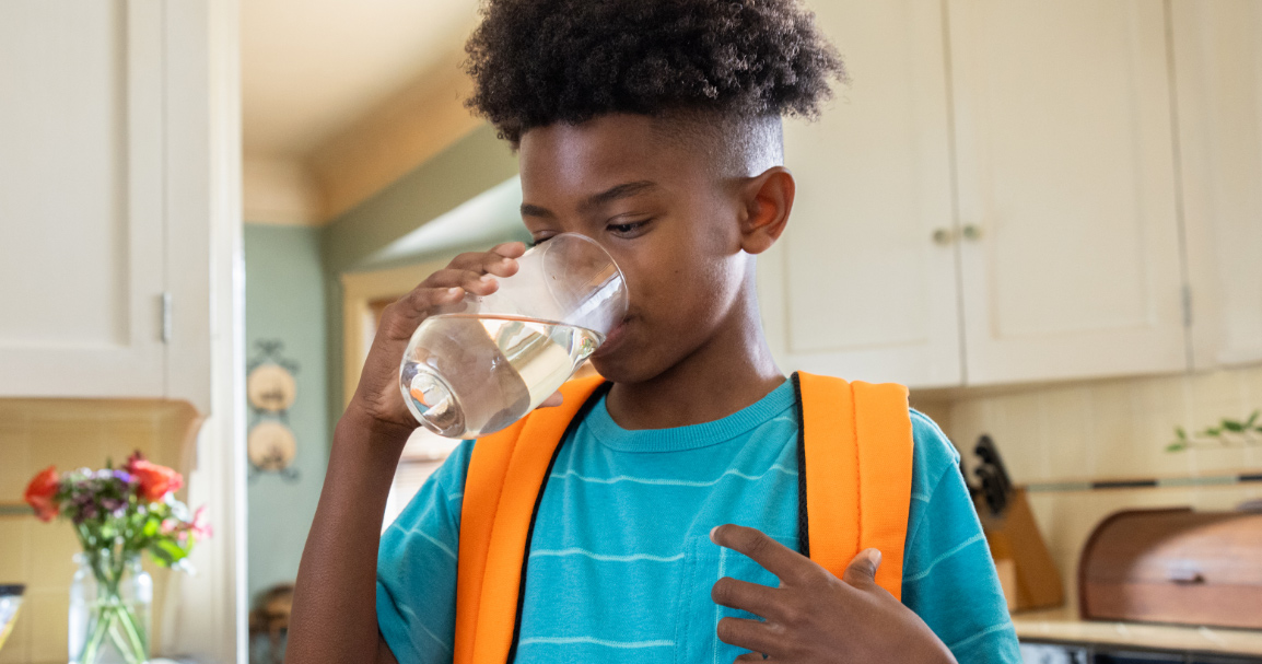 Un niño bebiendo agua de un vaso para saciar su sed.