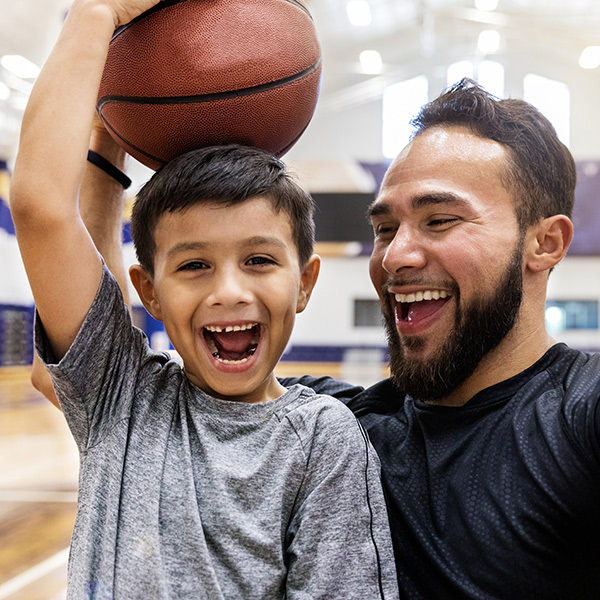 Un padre y su hijo juegan basketball, motivando a los niños a mantenerse activos y divertirse en familia.